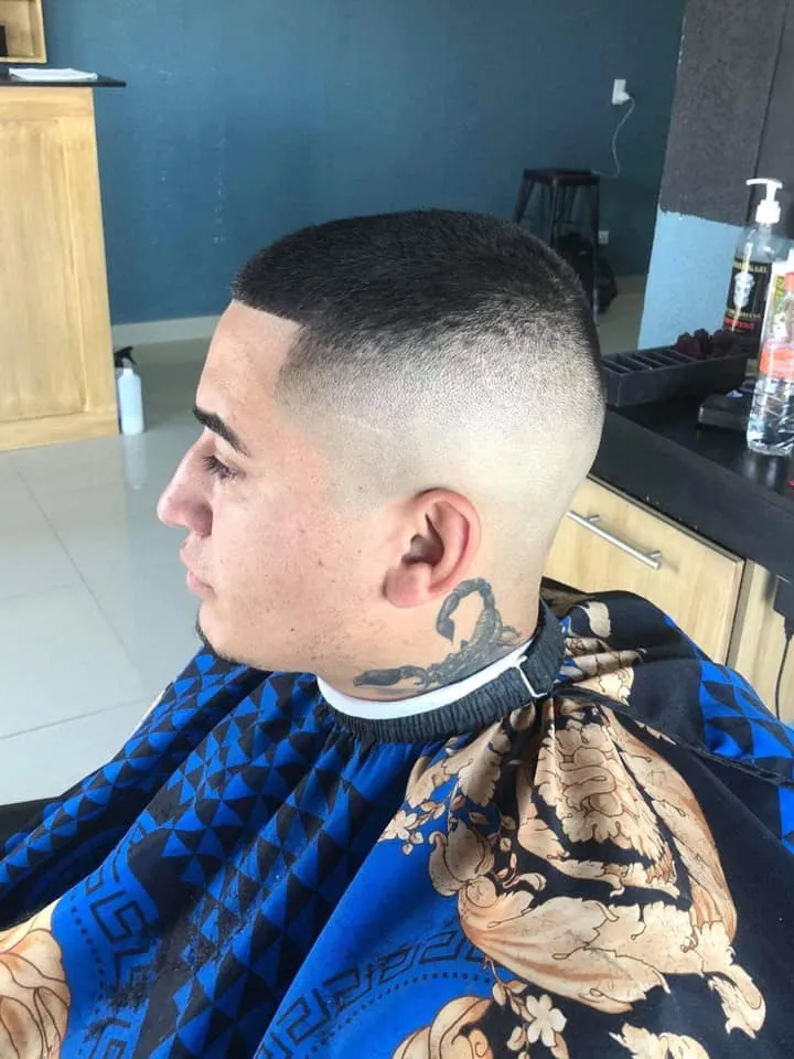 Un hombre con un corte de pelo muy corto y un tatuaje de un escorpión en la oreja.